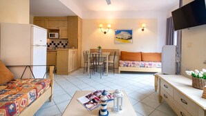 A compact living space with a kitchenette, a dining table, a sofa, a TV, and a ceiling fan.
