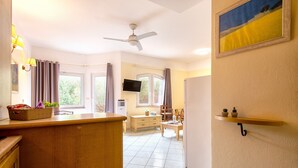 A room with a kitchen area, a dining table, a TV, and a ceiling fan.