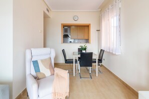 Un salon avec un canapé, une table à manger avec des chaises, un coin cuisine avec des placards et une horloge au mur.