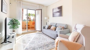 A modern living room with a sofa, a television, a plant, and a view of the outdoors.