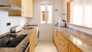 A compact kitchen with a built-in stove, microwave, and sink, wooden cabinets, and a window with a view.