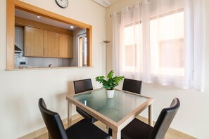 Un coin repas comprenant une table en verre, quatre chaises, une plante en pot, une horloge murale et une fenêtre avec des rideaux.