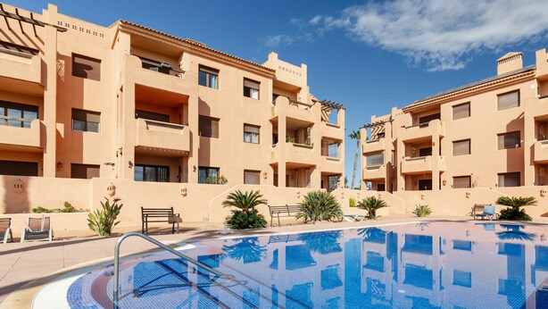 A swimming pool surrounded by a building with balconies and a clear sky.