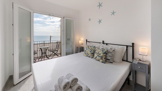 A bedroom with a bed, a nightstand, a table with chairs, and a balcony with a view. - Apartment 'Profumo Di Salsedine' with Sea View, Wi-Fi and Air Conditioning (Bonassola)