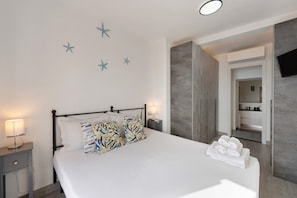 A neatly made bed with patterned pillows, a bedside table with a lamp, and a wall-mounted TV.
