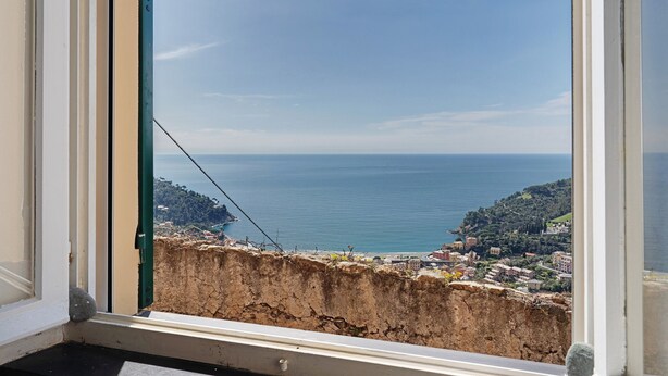 A coastal view from a window, including a cliff, ocean, and distant buildings.