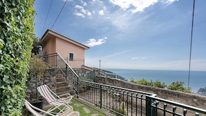 A house with a stone staircase, a balcony with a railing, and a view of the sea.
