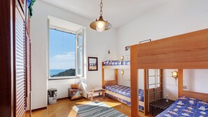 A room with bunk beds, a window with a view, a wooden ceiling, and a hanging light fixture.
