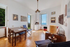 A room with a dining table, chairs, a bed, a TV, and artwork on the walls.