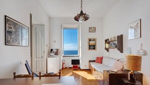 A room with a wooden table, a sofa, a TV, a lamp, and a window with a view.