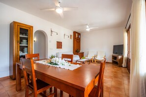 A dining area with a wooden table and chairs, a ceiling fan, and a television in the background.