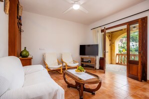 A living room with a sofa, two chairs, a coffee table with fruit, a TV, and a balcony with a view.