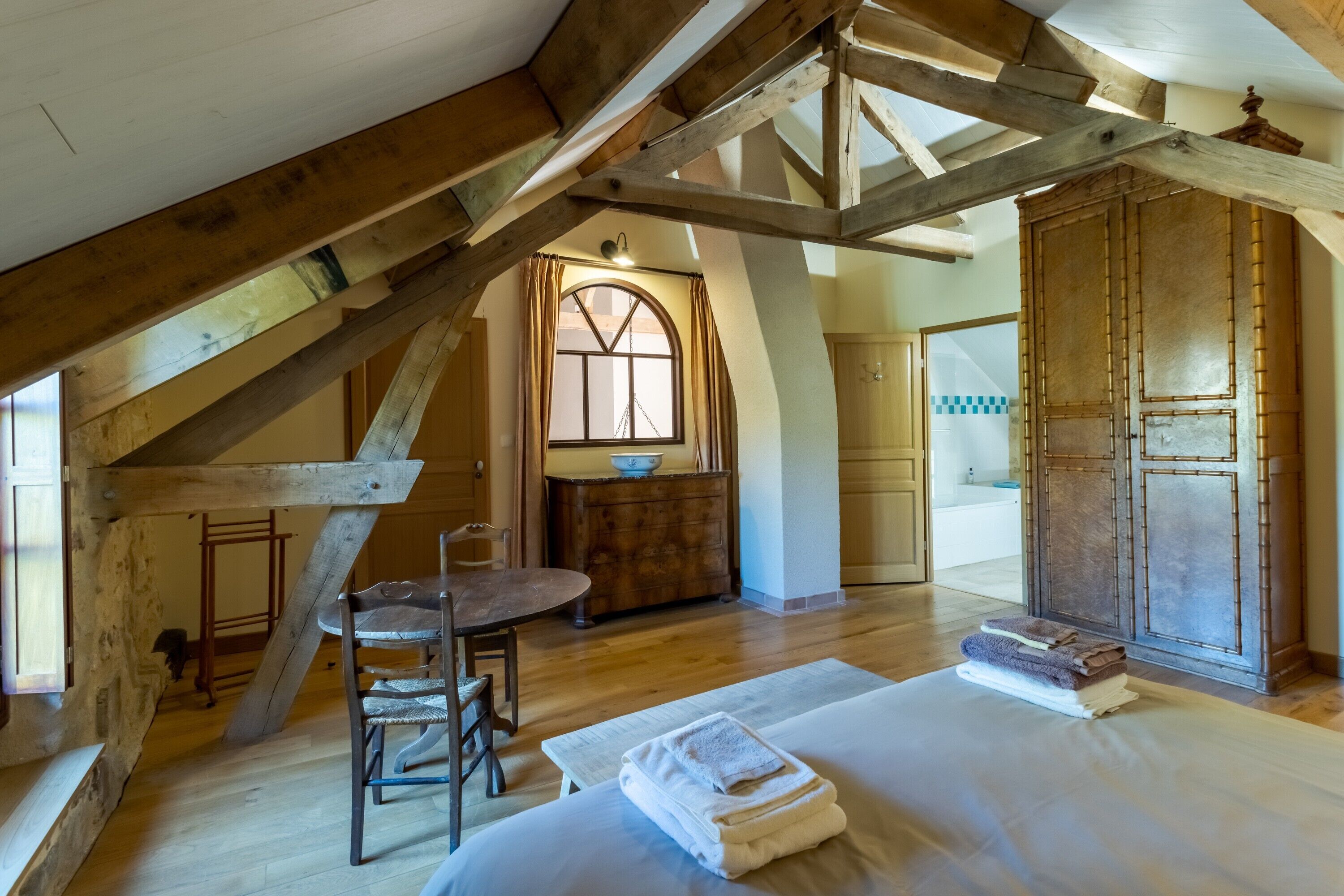 A rustic attic bedroom with exposed wooden beams, a wooden dining table, and a large wardrobe.