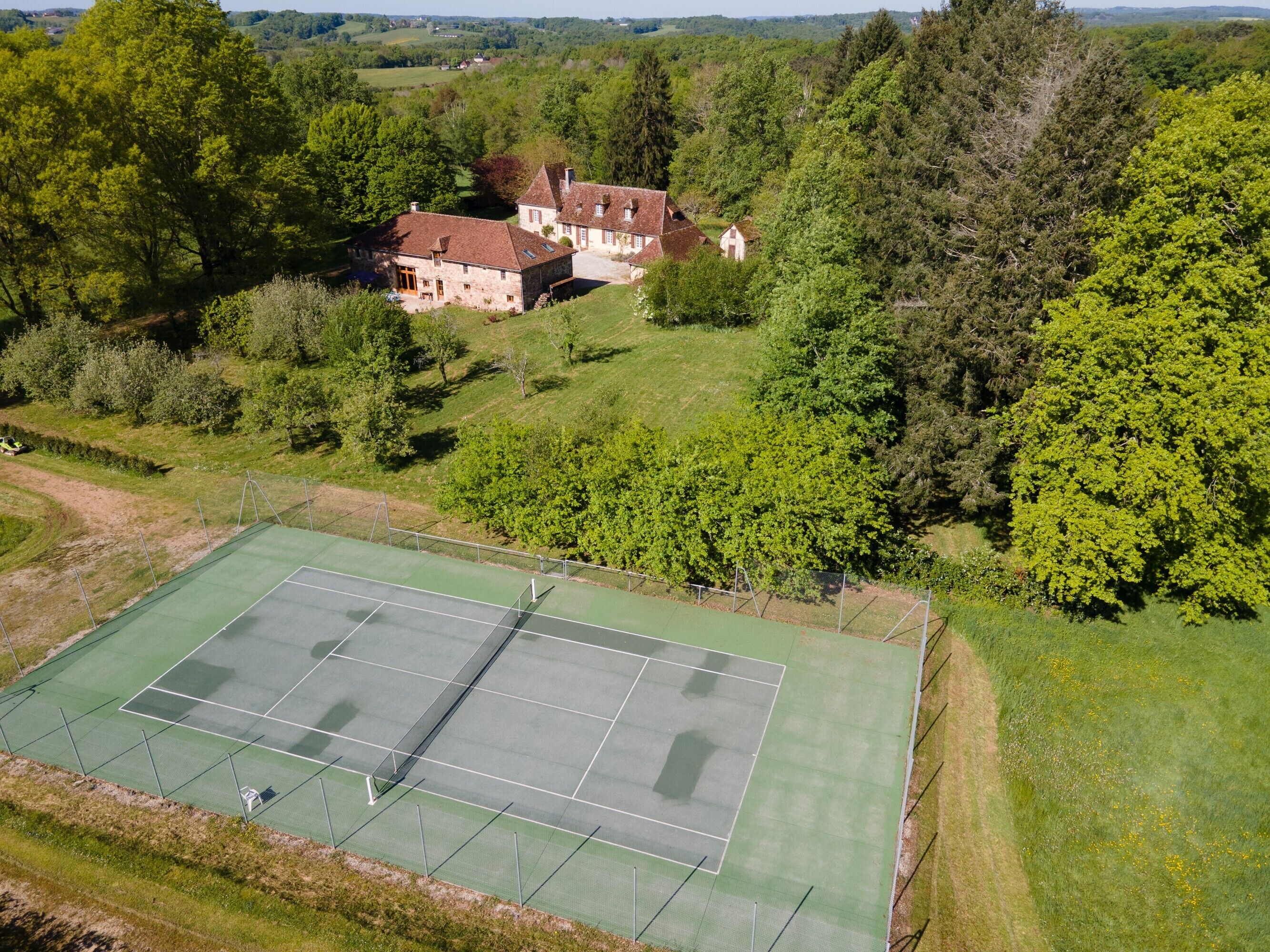 Ein Tennisplatz, umgeben von üppigem Grün und einem Steinhaus.