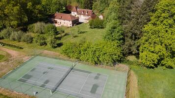 Ein Tennisplatz, umgeben von üppigem Grün und einem Steinhaus.