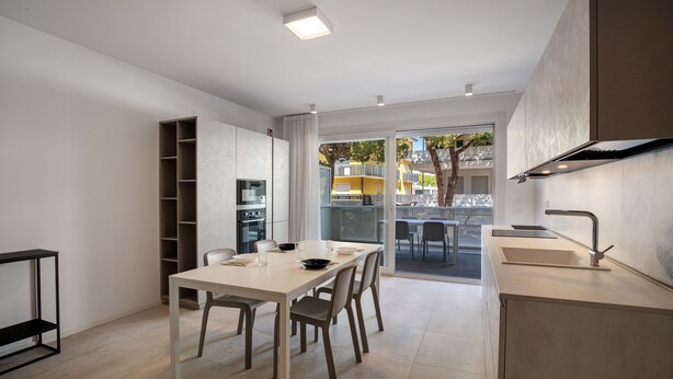 A modern kitchen with a dining area, built-in shelving, and a view of the outside. - Apartment 'Berton' with Private Terrace, Balcony, and Air Conditioning (Jesolo)