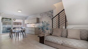 A modern living room with a sofa, dining table, chairs, and a kitchen area. - Apartment 'Berton' with Private Terrace, Balcony, and Air Conditioning (Jesolo)
