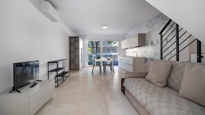 A modern living room with a flat-screen TV, a sofa, a dining table with chairs, and a staircase. - Apartment 'Berton' with Private Terrace, Balcony, and Air Conditioning (Jesolo)
