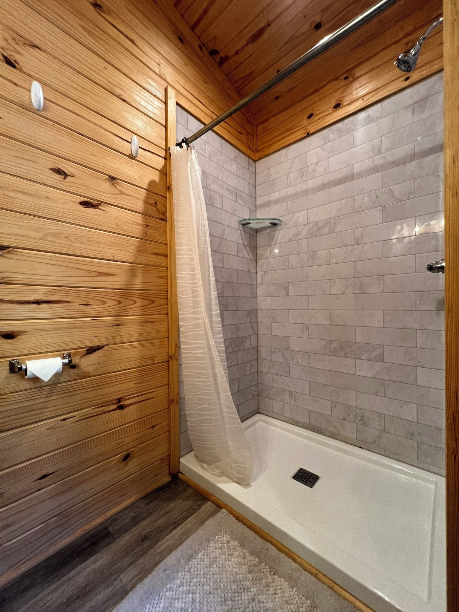 A wooden-paneled bathroom with a shower area, a towel rack, and a glass shower seat.