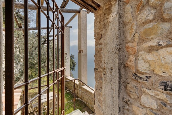 Un escalier en pierre mène à un balcon doté d’une rambarde en métal, d’où l’on peut admirer un paysage montagneux.