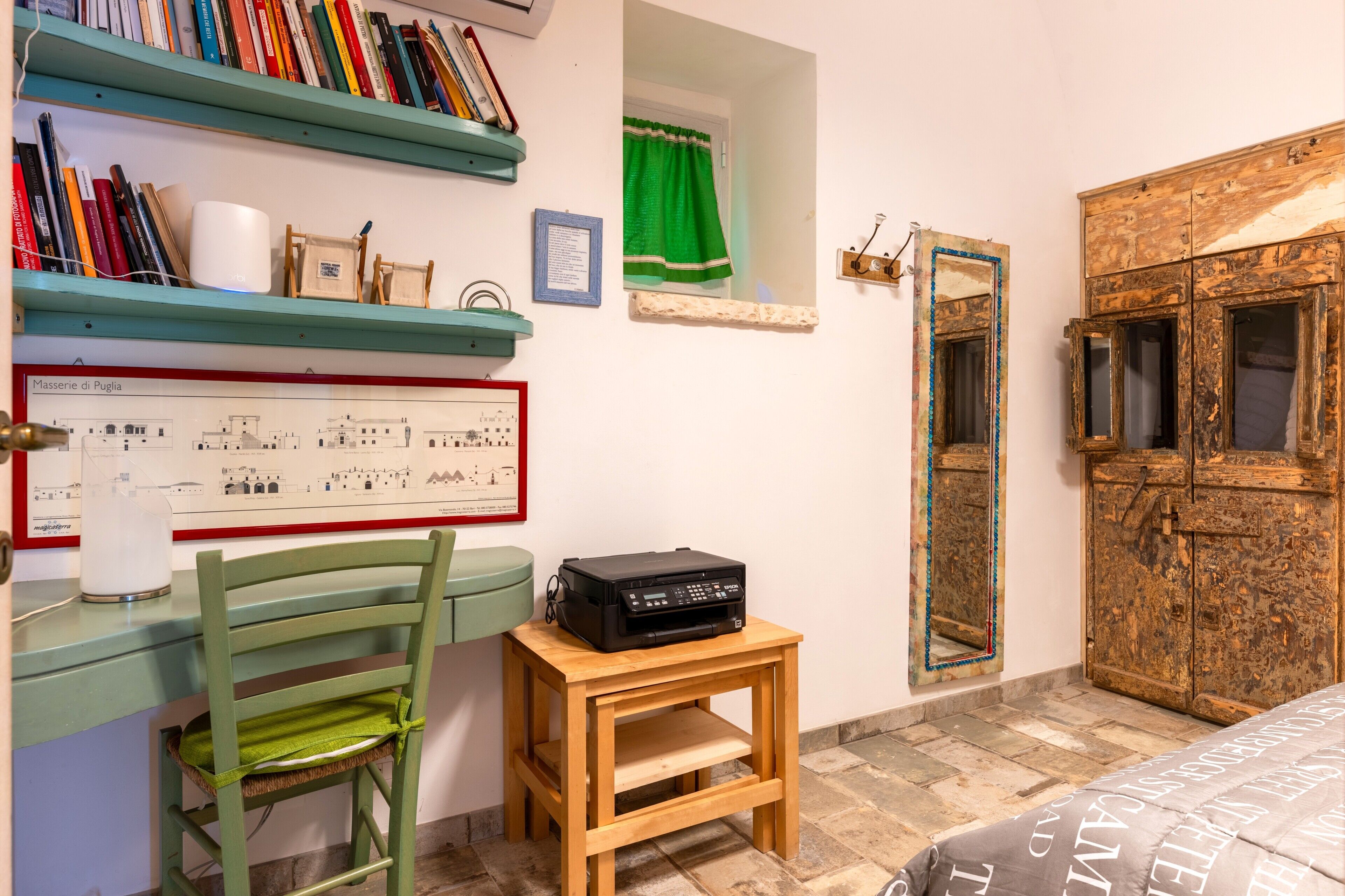 Una habitación con un escritorio de madera, una silla, una impresora, una estantería, un mapa enmarcado, un espejo y un armario de madera.