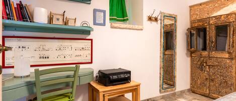 Una habitación con un escritorio de madera, una silla, una impresora, una estantería, un mapa enmarcado, un espejo y un armario de madera.