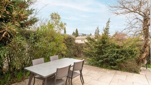 An outdoor patio with a table and chairs, surrounded by greenery and a view of a building in the distance. - Air-conditioned villa with pool in Vaison-la-Romaine, in the heart of Provence (Vaison-la-Romaine)