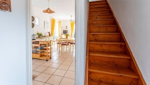 A wooden staircase leading to a room with a tiled floor, a dining area with a table and chairs, and a kitchen area with a cart and cabinets. - Air-conditioned villa with pool in Vaison-la-Romaine, in the heart of Provence (Vaison-la-Romaine)