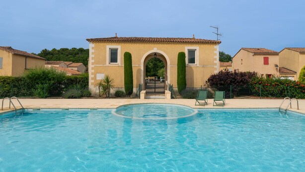 A swimming pool with a clear view of the poolside area, a building with an arched entrance, and a few surrounding houses. - Air-conditioned villa with pool in Vaison-la-Romaine, in the heart of Provence (Vaison-la-Romaine)
