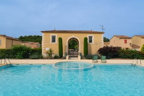 Uma piscina com vista clara da área da piscina, um edifício com entrada em arco e algumas casas próximas.