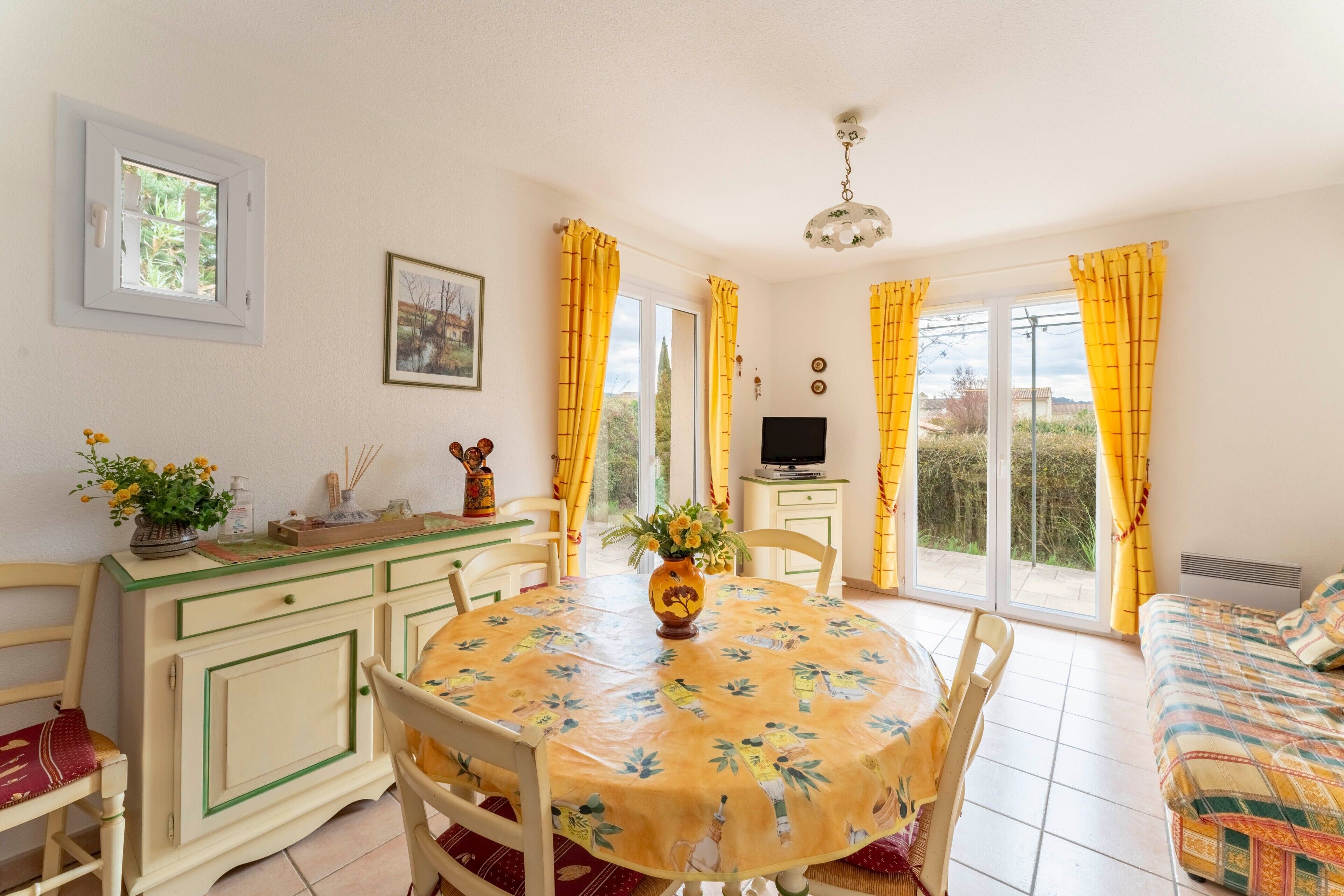 A room with a dining table, chairs, a sofa, a TV, and a window with curtains.