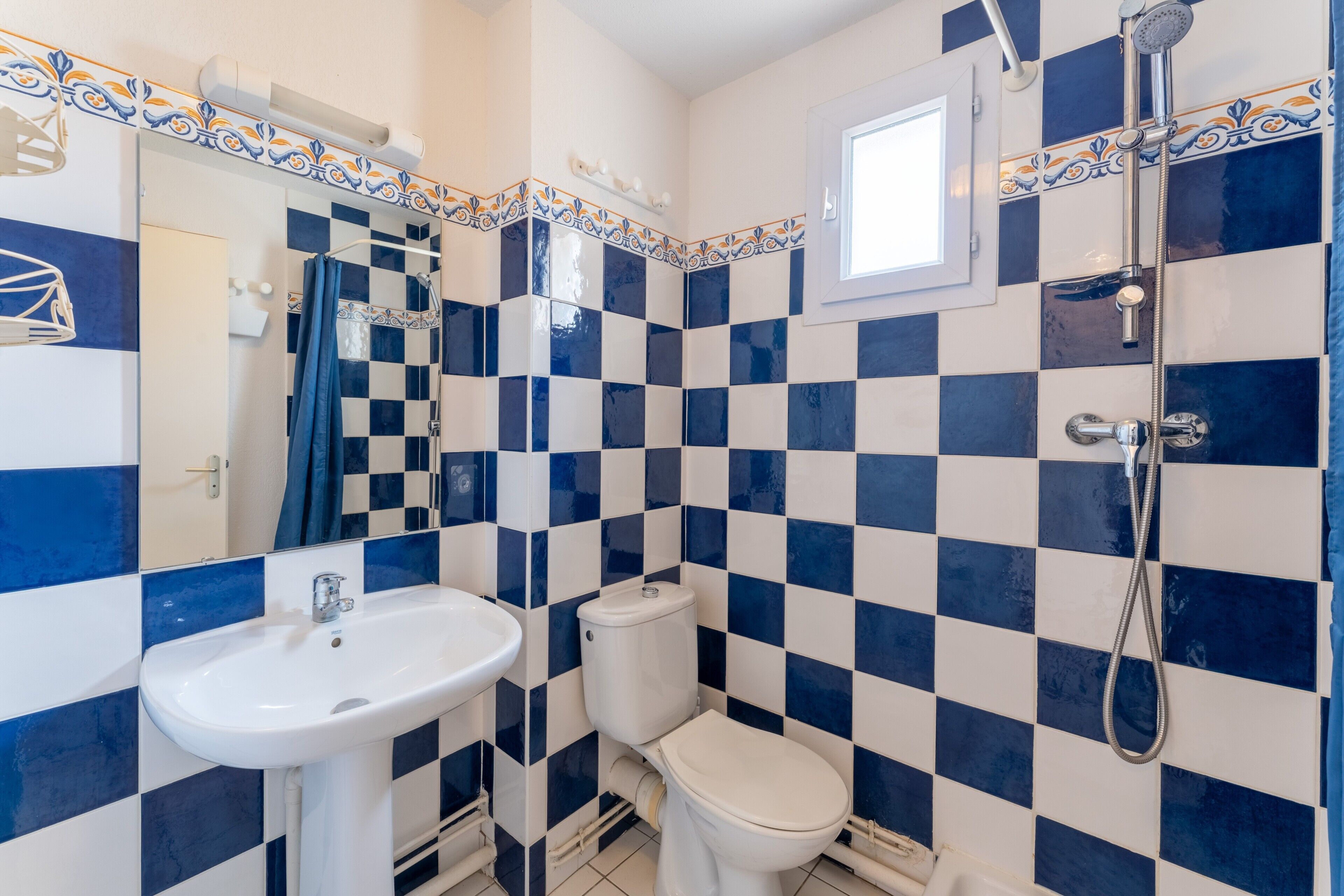 A bathroom with a checkered tile pattern, a sink, a toilet, and a shower.