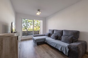 A modern living room with a grey sectional sofa, a wooden cabinet, and a large window with a view of trees.