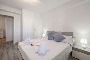 A neatly made bed with towels and a rose, a bedside lamp, and a door leading to another room.
