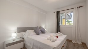 Una cama bien hecha con almohadas, una lámpara de noche y una ventana con cortinas.