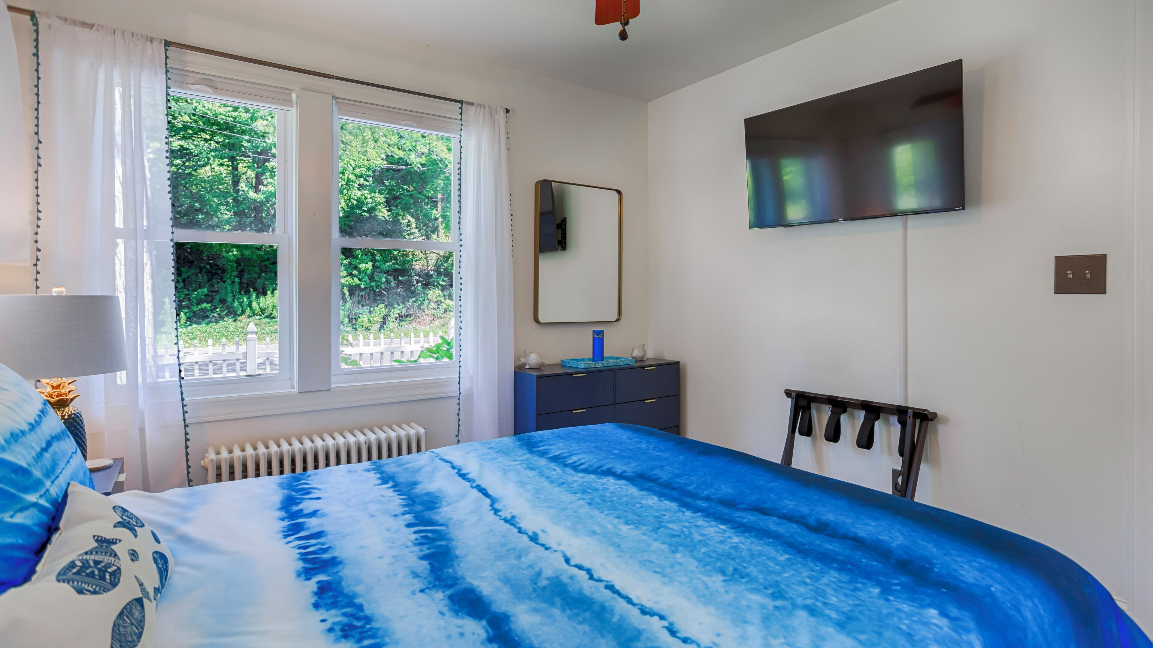 A bedroom with a large bed, a dresser, a mirror, and a TV on the wall.
