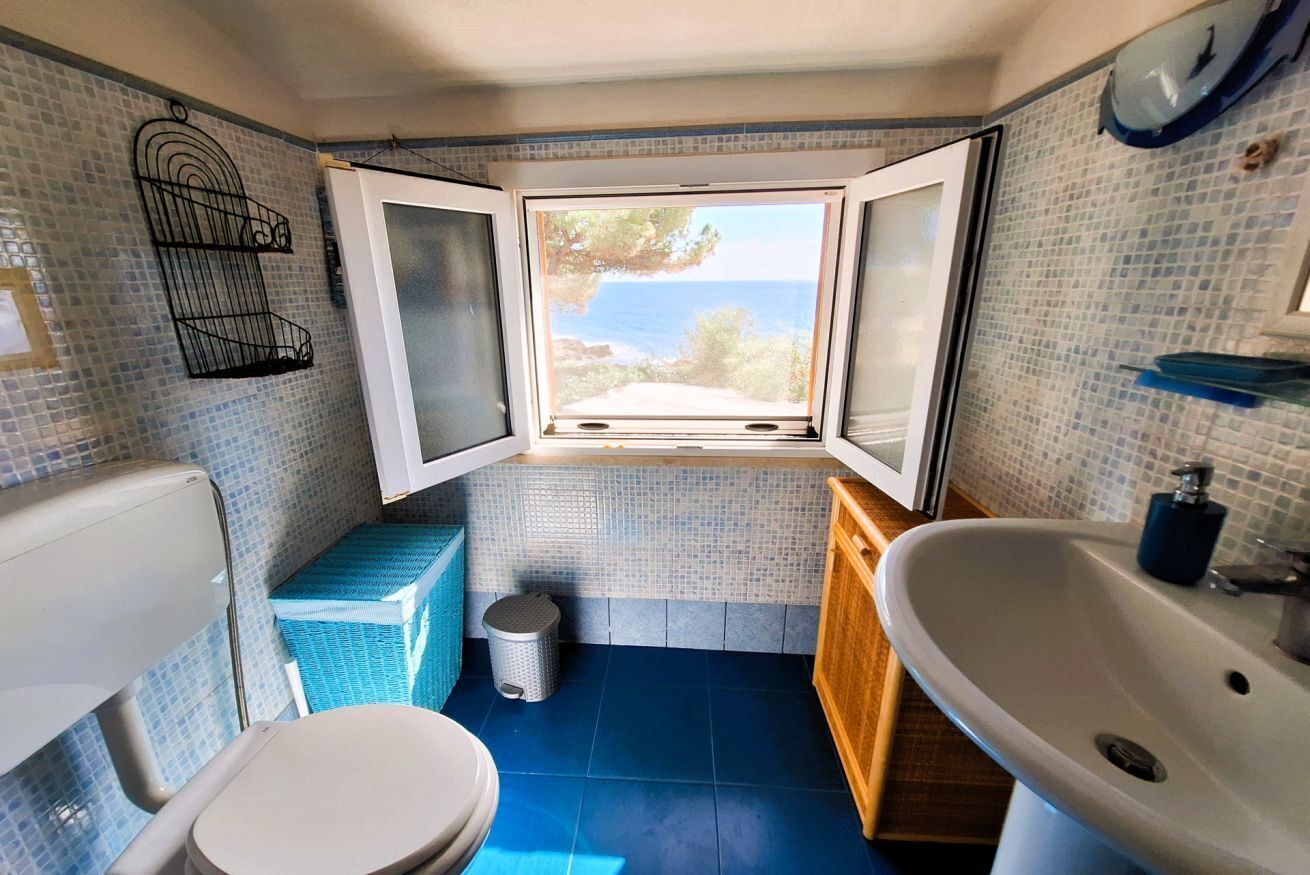 A compact bathroom with a view of the sea, a white sink, and a toilet.