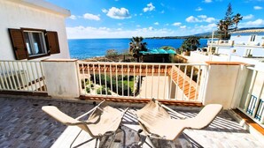 A balcony with two beige lounge chairs, a white railing, and a view of the sea and distant hills. - VILLA THE HELM - ORTIGIA HOLIDAYS (Fontane Bianche)