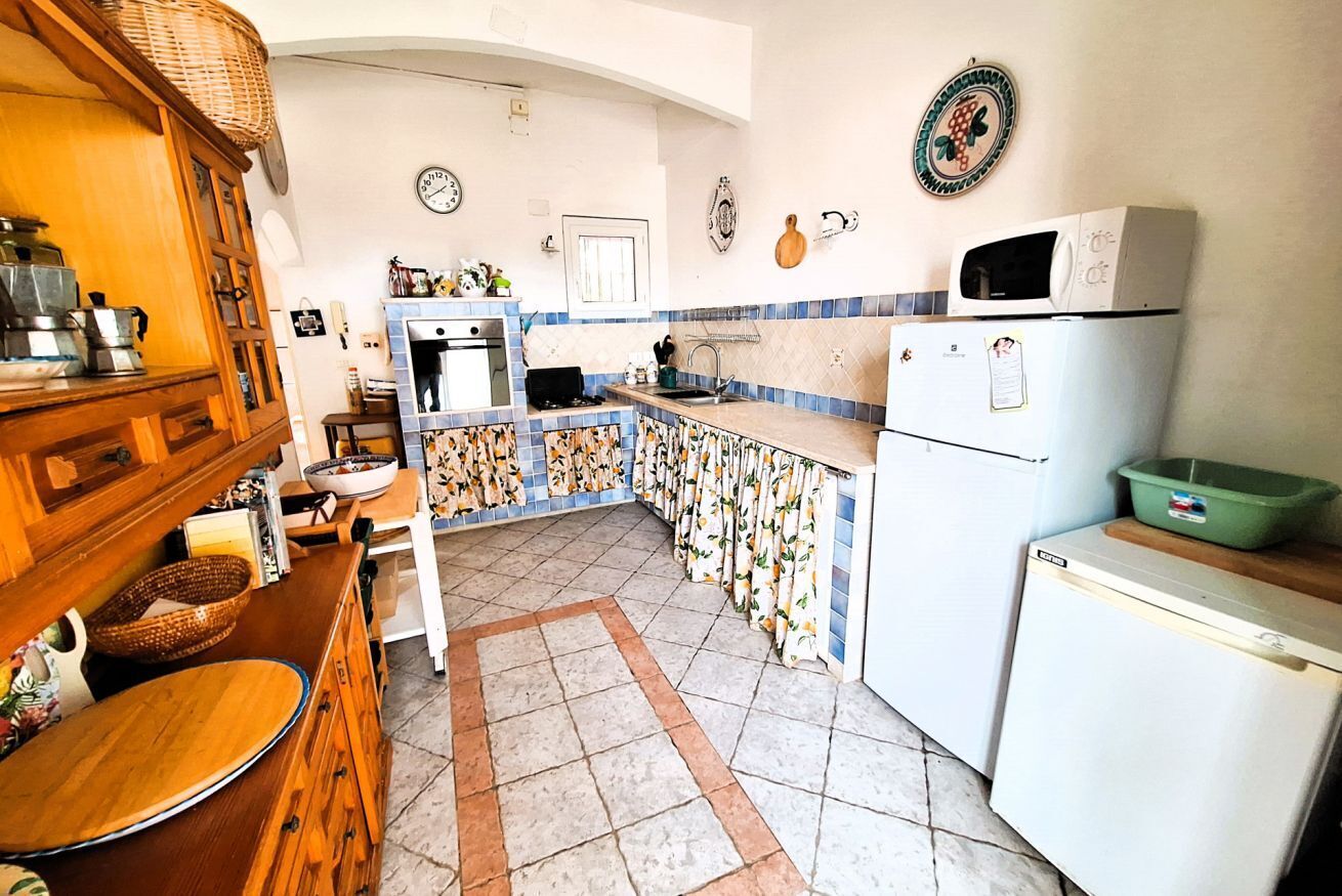 Uma cozinha compacta com fogão, pia e geladeira. Há pratos decorativos na parede e um armário de madeira.