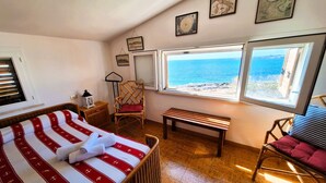 A bedroom with a bed, a chair, a bench, and a view of the sea through large windows. - VILLA THE HELM - ORTIGIA HOLIDAYS (Fontane Bianche)
