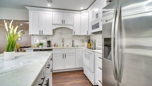A modern kitchen with white cabinets, a stainless steel refrigerator, and a marble countertop. - Home Close to Saint Pete Pier new Spacious (St. Petersburg)