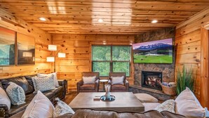 Ein gemütliches Blockhaus-Interieur mit Kamin, Ledersofas und einem großen Fenster mit schöner Aussicht.