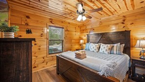 Ein Schlafzimmer einer Holzhütte mit Bett, Deckenventilator, Fenster und Nachttisch.