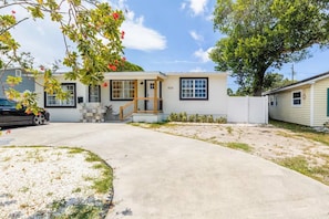 A single-story house with a front porch, a small patio, and a driveway leading to a parked car. - 10 min to St Pete Beach w/ Parking - 1BD 1BA (St. Petersburg)