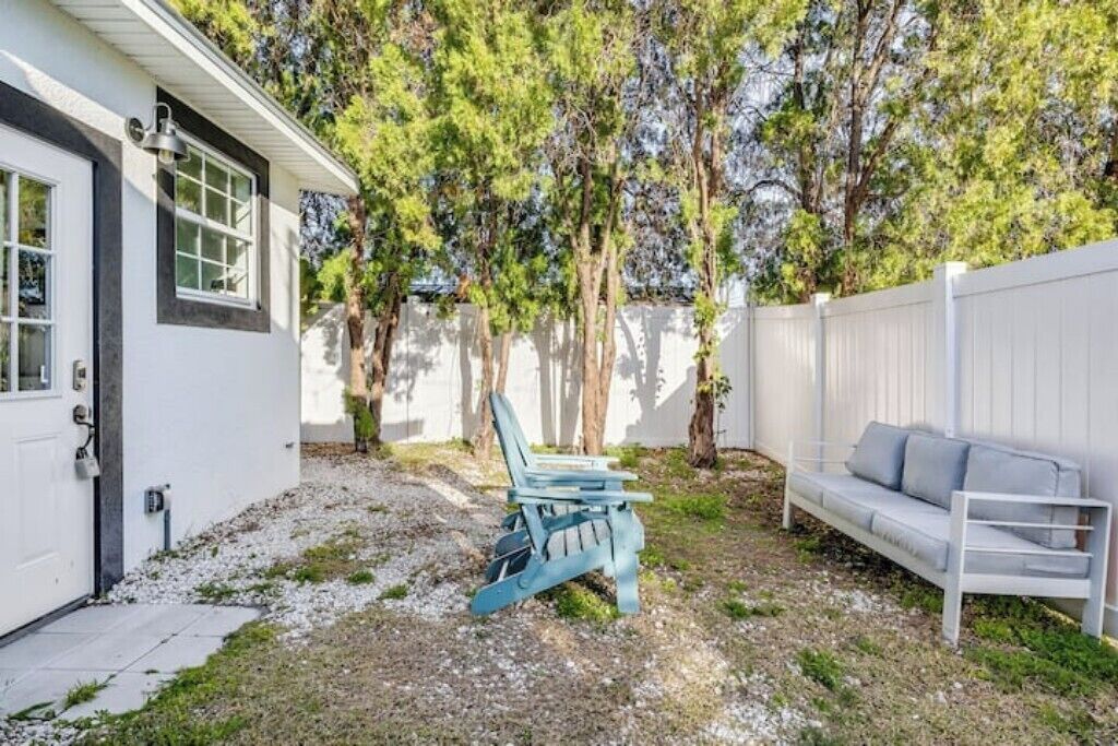 Un patio trasero con valla blanca, una silla Adirondack azul y un sofá blanco.