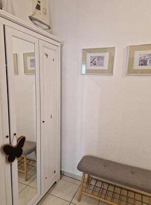 Ein Zimmer mit einem weißen Kleiderschrank, einer Bank und gerahmten Bildern an der Wand.