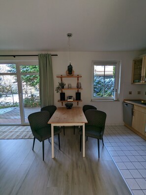 Ein Essbereich mit einem Holztisch, vier Stühlen, einem Regal mit Dekoration und Blick ins Freie durch große Fenster.