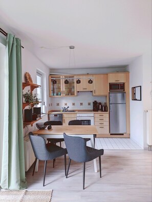 A modern kitchen with wooden cabinets, a stainless steel refrigerator, and a dining area with two chairs.