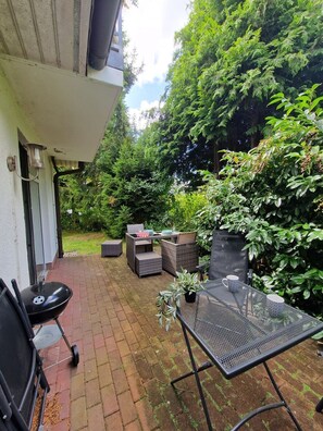 Eine Terrasse mit Grill, Gartenmöbeln und einem Tisch mit Tassen.