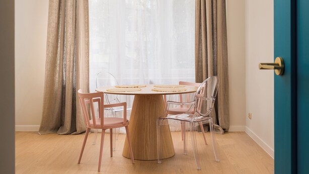 A dining area with a round wooden table, four chairs, and a view through sheer curtains. - Metro Młynów Colourful Apartment (Warszawa)